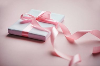 Süslü beyaz hediye kutusu pembe kurdeleli ve pembe arka planda uzun güzel bir kurdele.