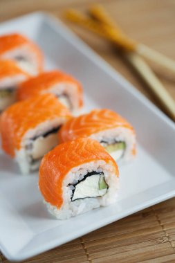 Peynirli, avokadolu ve beyaz tabakta somonlu lezzetli suşi rulosu. Bulanık arkaplan