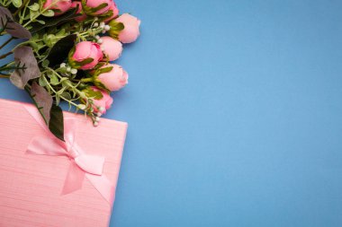 Güzel çiçekli kompozisyon ve mavi arka planda pembe hediye kutusu. Düz yatıyordu. Üst Manzara. Metin için yer.