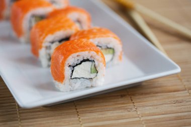 Philadelphia beyaz tabakta somon, avokado ve krem peynirli suşi sarıyor. Suşi menüsü. Japon yemeği..