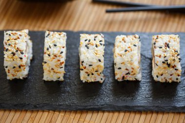 Uramaki siyah tahta çubuklarla siyah bir levhada hizmet verdi. Bambu servisli geleneksel Japon yemekleri..