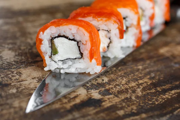 Philadelphia sushi roll with sushi knife on wooden background. Sushi menu. Japanese cuisine.