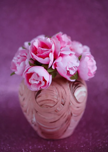 Piękne małe różowe kwiaty w małym wazonie z wzorem na ciemnym różowym, błyszczącym tle — Zdjęcie stockowe