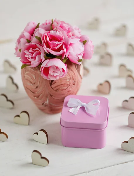 Hermosa composición con pequeña caja de regalo cuadrada metálica rosa y delicadas rosas en jarrón rosa sobre fondo de madera blanca — Foto de Stock