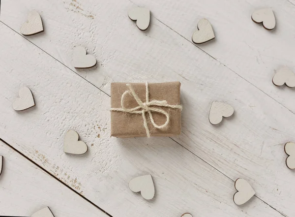 Regalo pequeño envuelto en papel rosa, corazones decorativos alrededor del regalo sobre fondo blanco . —  Fotos de Stock