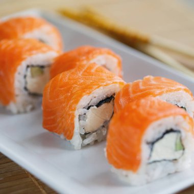 Somon, avokado ve peynirli suşi, beyaz tabakta hazır. Suşi menüsü. Japon yemeği..