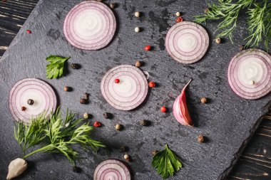 Kırmızı soğan halkaları, sarımsak, dereotu ve baharatlar tahtada. Üst görünüm.