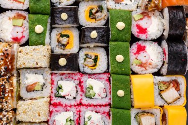 Taştan arka planda çeşitli suşiler. Farklı dolgulu büyük renkli rulo. Somon, ton balığı, yılan balığı, avokado, salatalık, Philadelphia peyniri, pirzola ve havyar. Görüntüyü kapat.