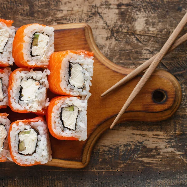 日本菜 寿司配上费城奶酪 鳄梨和鲑鱼 放在棕色木板上 — 图库照片