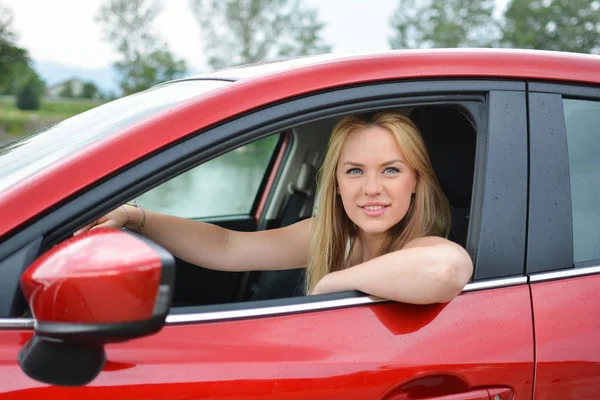 Giovane ragazza bionda sorridente e soddisfatta in auto rossa — Foto Stock