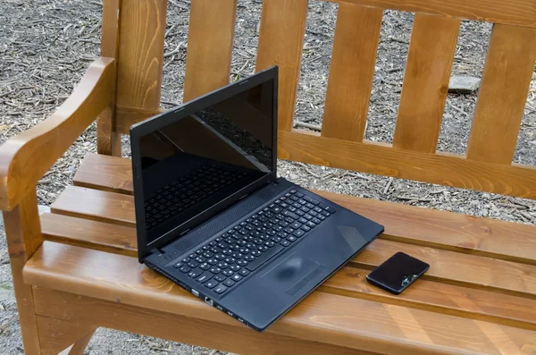 Open laptop computer and phone on a wooden bench