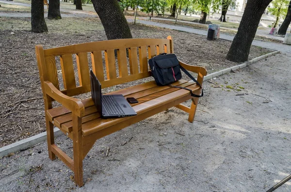 Otwórz laptopa, torby i telefon na ławeczce, drewniane — Zdjęcie stockowe