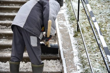 Kadın temizlikçi sokak merdivenlerinden kar kürüyor.