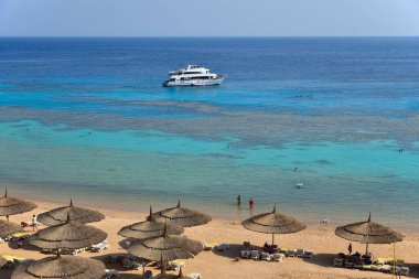 Mısır 'da mercan resifinin yanında turistlerin olduğu bir otel kumsalı, dalgıçlı bir yat..