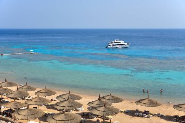 Mısır 'da mercan resifinin yanında turistlerin olduğu bir otel kumsalı, dalgıçlı bir yat..