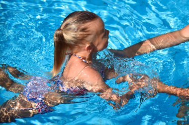 Anne bir çocuğa havuzda yüzmeyi öğretiyor..