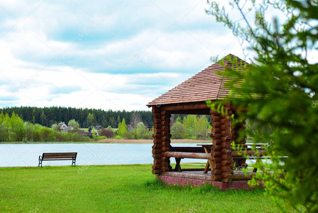 Wooden arbor with a bench on the shore of a forest lake.