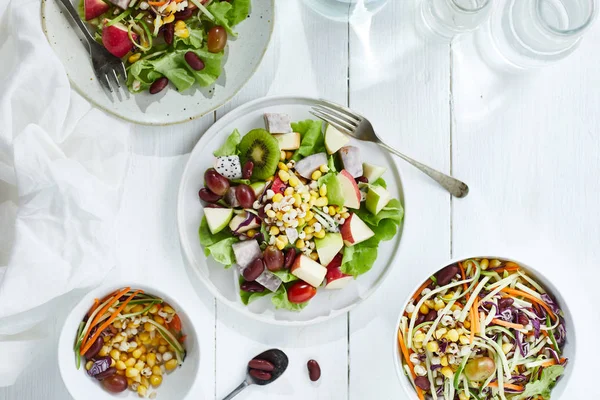 Deliciosa ensalada de frutas y diferentes frutas en la mesa blanca, h —  Fotos de Stock