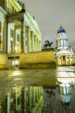 Ünlü Gendarmenmarkt ışıklı Berlin konser salonu ve Fransız Katedrali ıslak zemin üzerinde yağmur sonrası alacakaranlık günbatımı sırasında Berlin şehir merkezinde yansıtan kare panoramik manzaralı
