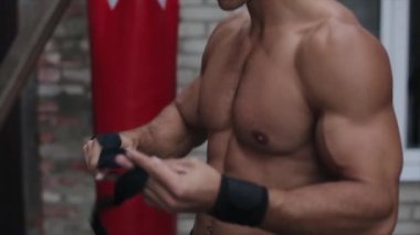 Siyah bir boks bandajıyla eli saran üstsüz, kaslı adamın yakın görüntüsü.