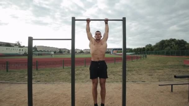 Подходящий молодой человек делает подвешенную ногу поднимает упражнения на горизонтальном баре в уличном спортзале — стоковое видео