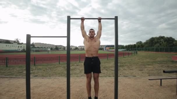 Fit young man doing hanging leg raises exercise on horizontal bar in the street gym — Stock Footage Fit young man doing hanging leg raises exercise on horizontal bar in the street gym Stock Footage