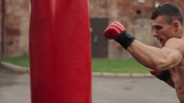Близкий вид боксера в красных перчатках, ударяющего красную боксерскую грушу на улице — стоковое видео