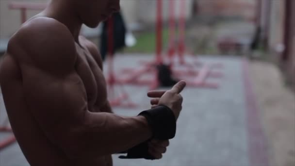 Fechar vista do homem muscular sem camisa que envolve a mão com bandagem de boxe preto — Vídeo de Stock