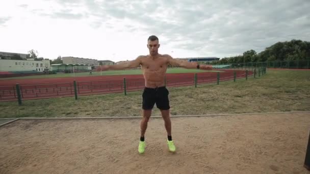 Bonito atleta masculino fazendo exercícios de macaco de salto enquanto treina no estádio ao ar livre — Vídeo de Stock