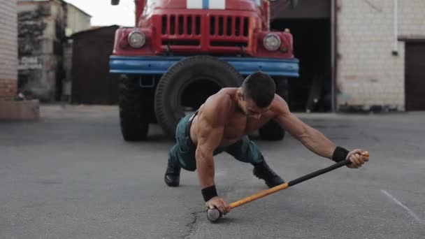 Muscular handsome sportsman doing push-ups with a sledgehammer in front of a fire engine — Stock Video