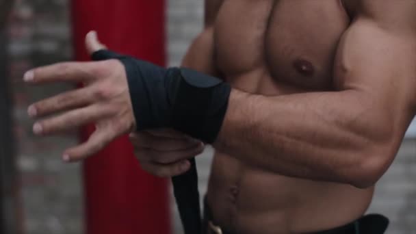 Siyah bir boks bandajıyla eli saran üstsüz, kaslı adamın yakın görüntüsü. — Stok video