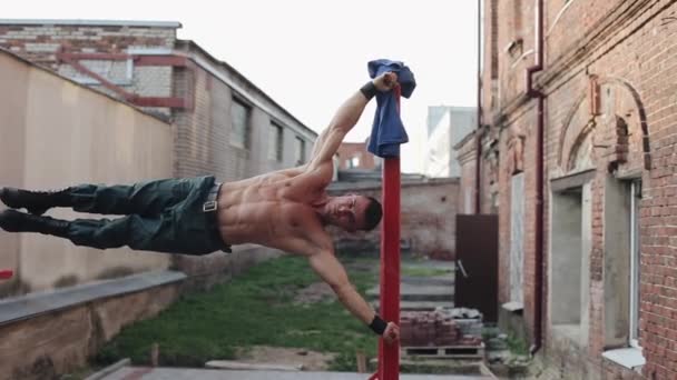 Un apuesto deportista fuerte haciendo ejercicio en las barras rojas fuera — Vídeos de Stock