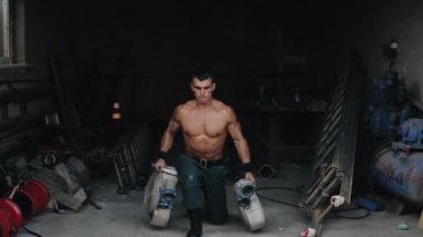 Yakışıklı üstsüz bir itfaiyeci iki elinde de yangın hortumu tutarak saldırıyor. Arka planda itfaiye ekipmanları