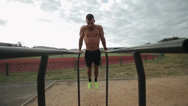Esportista bonito fazendo flexões em barras paralelas no estádio ao ar livre — Vídeo de Stock