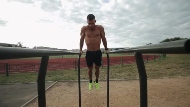 Good-looking sportsman doing push-ups on parallel bars on the outdoor stadium — Stock Footage Good-looking sportsman doing push-ups on parallel bars on the outdoor stadium Stock Video