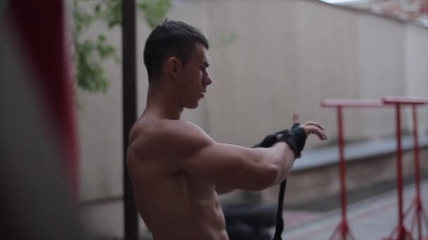 Близкий взгляд на мускулистого мужчину, обертывающего руку черной боксерской повязкой — стоковое видео