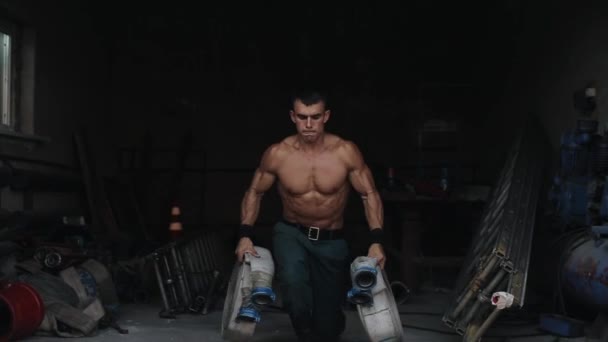 A handsome shirtless firefighter doing lunges holding a firehose in each hand. Fire-fighting equipment on the background — Stock Video