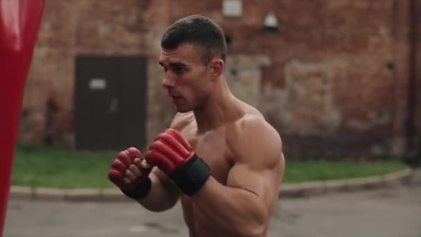 Langzame beweging. Goed zicht. man shirtloos bokser raken van een Groot boksbal met zijn vuisten tijdens de straat workout — Stockvideo