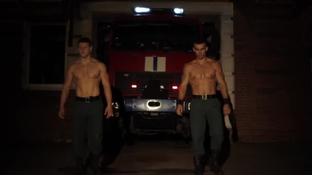 Two muscular shirtless sportsmen doing extreme push-ups in front of a fire truck with flashing emergency lights and sirens at night outdoor — ストック動画