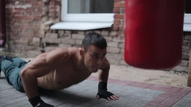 Όμορφος αθλητής κάνει ακραίες push-ups με το χτύπημα το σάκο του μποξ. Κλείσιμο προβολής — Αρχείο Βίντεο