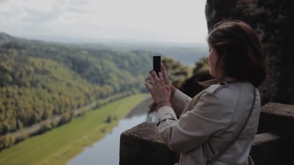 Dresden, Duitsland - 12 augustus 2019: Mooi jong meisje dat op haar smartphone foto 's maakt van prachtige bergen. Sluit zijaanzicht. Meisje staat hoog met berg rivier beneden. — Stockvideo