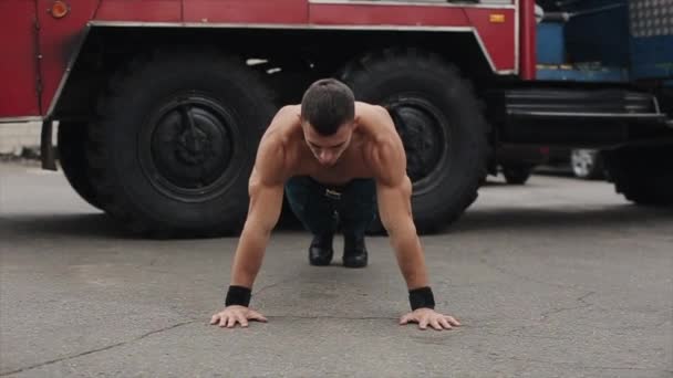 Guapo joven deportista haciendo flexiones con aplausos al aire libre con un camión de bomberos en el fondo — Vídeos de Stock