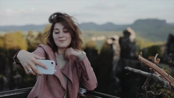 Bella giovane donna scatta foto di se stessa in montagna, sorrisi e onde. Al rallentatore. Vista da vicino. Sfondo sfocato. Bastei. Parco nazionale della Svizzera sassone — Video Stock