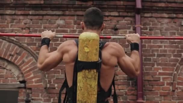 Voltar vista de perto do bombeiro sem camisa muscular com tanque de oxigênio em suas costas fazendo exercícios na barra horizontal ao ar livre — Vídeo de Stock