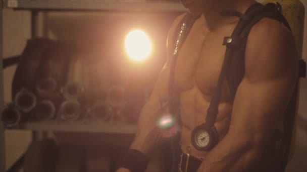 Zeitlupe. Nahaufnahme. Hemdloser gutaussehender Mann mit Sauerstofftank und Manometer setzt Sauerstoffmaske auf. heller Projektor im Hintergrund — Stockvideo