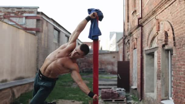 Мускулистый топлесс молодой парень делает гимнастику на вертикальном красном баре на открытом воздухе — стоковое видео