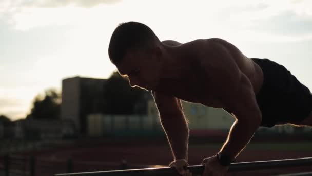 Uma visão lateral close-up de um jovem fisiculturista muscular bombeando os braços com uma barra — Vídeo de Stock