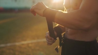 Siyah bilek desteği takan kaslı bir sporcunun yakın görüntüsü. Arkaplanda parlak güneş