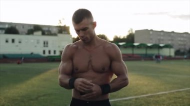 Siyah bilek desteği takan kaslı bir sporcunun yakın görüntüsü. Arkaplanda parlak güneş
