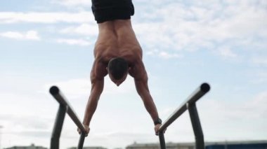 Spor sahasında vücut ağırlığı şınavı yapan üstsüz bir sporcunun yakın görüntüsü. Arka planda futbol oynayan insanların bulanık görüntüsü